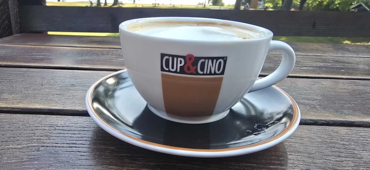 Cappuccino auf einem Holztisch mit Blick ins Strandbad St. Alban
